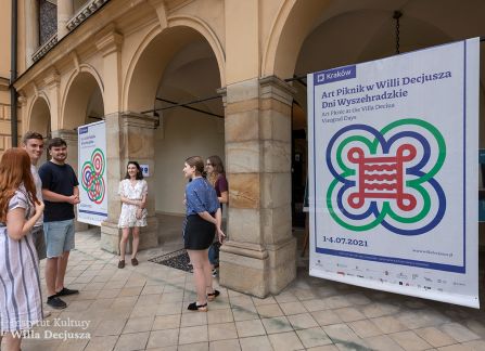 fotografia. goście festiwalu art piknik przed willą decjusza. w tle bannery promujące festiwal rozpięte między kolumnami arkad na fasadzie willi.